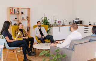 three women and two men sitting around a table on chairs and couch talking