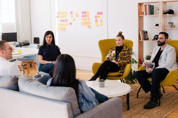 four people seated around table with whiteboard covered in notes behind them