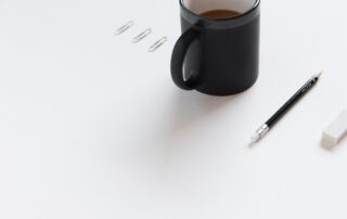 white desk with three paperclips, cup of coffee, pencil, and eraser lined up neatly