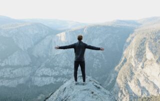 man standing on top of mountain with hands stretched out