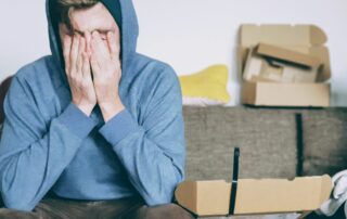 business owner with head in hands surrounded by boxes looking burnt out